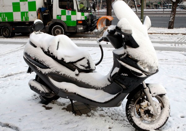 Una moto aparcada cubierta de nieve en una calle de Madrid, que presenta hoy una estampa blanca, nada habitual en la capital,.