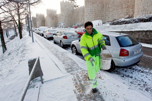 Un operario esparce sal junto a la muralla de Ávila para derretir la nieve que ha caído sobre la ciudad, al igual que en otras zonas del centro de la Península.