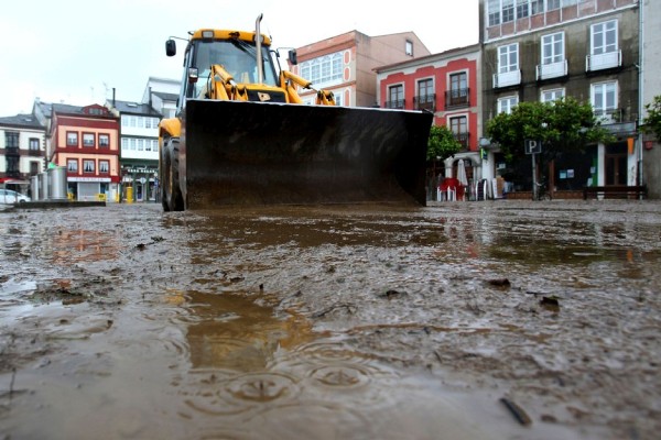 Una máquina excavadora retira el barro acumulado en la plaza de Vegadeo (Asturias) tras la riada causada por las intensas lluvias caídas en la región.