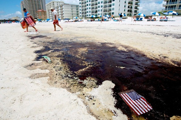 Dos personas caminan cerca de una bandera estadounidense adherida a una mancha de petróleo en una playa de Gulf Shores, Alabama, Estados Unidos.