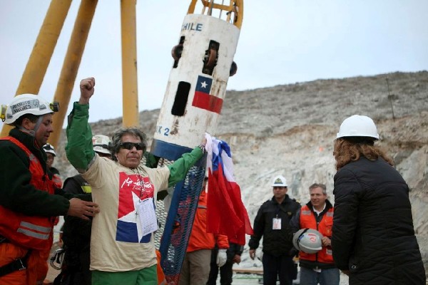 El minero Mario Gómez, de 63 años, el más delicado de salud, saluda con una bandera chilena en la mano al llegar a la superficie dentro de la cápsula Fénix, tras ser rescatado en noveno lugar hoy, 13 de octubre de 2010, en el yacimiento San José, donde se realizan las labores de rescate de los 33 mineros que permanecen atrapados desde el 5 de agosto.