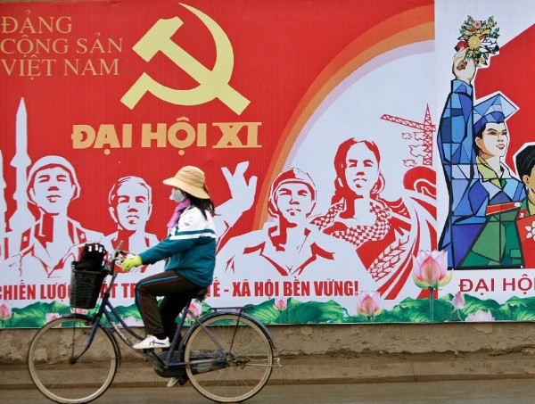 Una ciclista pasa con su bicicleta delante de un cartel promocional de la 11 edición del Congreso Nacional del Partido Comunista de Vietnam.