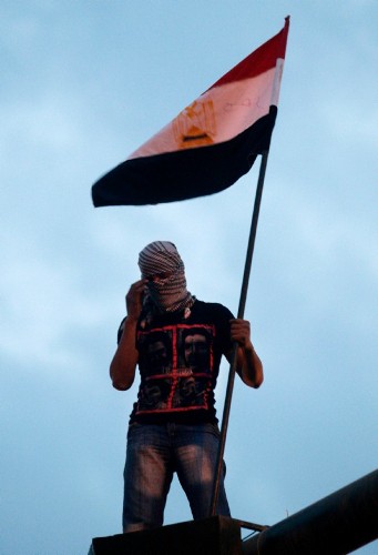 Un manifestante portando una bandera egipcia sobre un semáforo.