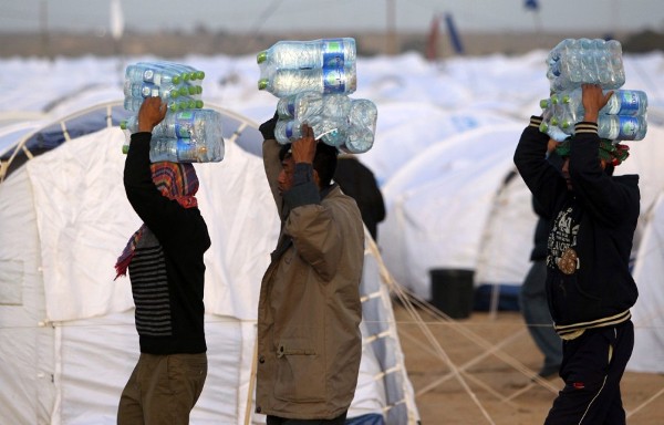 Trabajadores extranjeros que residían en Libia llevan agua en el campamento de ACNUR.