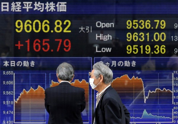 Dos ejecutivos japoneses caminan frente a una pantalla que muestra los valores de la Bolsa de Tokio.