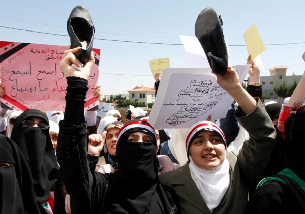 Manifestantes sirios residentes en Jordania sostienen sus zapatos y gritan consignas en contra del presidente de Siria.