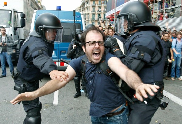 Dos policías intentan sujetar a una de las personas concentradas en la plaza Cataluña de Barcelona desde hace casi dos semanas y que los Mossos d'Esquadra han desalojado hoy en una operación que se ha saldado, por el momento, con más de cuarenta heridos y un detenido.