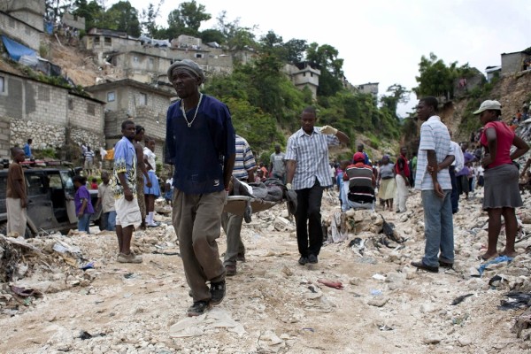 Tres hombres transportan el cuerpo de una mujer fallecida en una vivienda en Peguy Vile, Puerto Príncipe tras las lluvias.