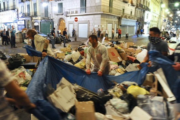 Ciudadanos que lucen máscaras en su boca y ropa de trabajo desechable blanca, mueven basura de los callejones del barrio español de Nápoles.