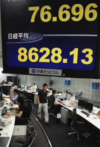 Corredores de bolsa trabajan bajo una pantalla que informa sobre el cambio del dólar al yen.