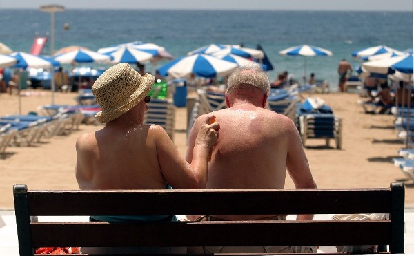 Una pareja de turistas se da crema solar junto a la playa de Benidorm esta mañana en el primer día de vacaciones.