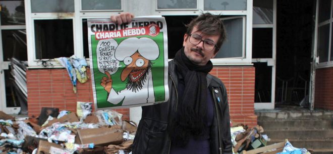Un periodista del semanario satírico Charlie Hebdo muestra la portada del último ejemplar en las afueras de las oficinas de la revista en París (Francia).