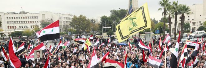 Centenares de simpatizantes del régimen de Bachar al Asad ondean banderas sirias.