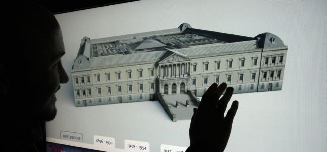 Sobre una pantalla táctil, un hombre busca información de la exposición que ha preparado la Biblioteca Nacional de España para conmemorar su tricentenario.