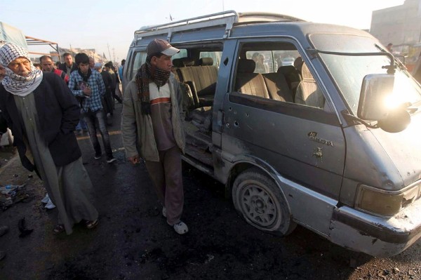 Civiles iraquíes junto a un vehículo alcanzado por la metralla.