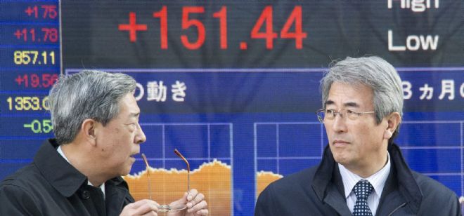Empresarios conversan frente a una pantalla con el cierre de la Bolsa de Tokio.