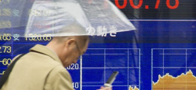 Un peatón camina frente a un tablero con los índices de la Bolsa de Tokio.
