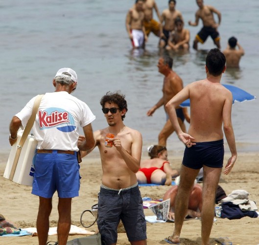 Varias personas compran refrescos a un vendedor ambulante en la playa de Las Canteras.