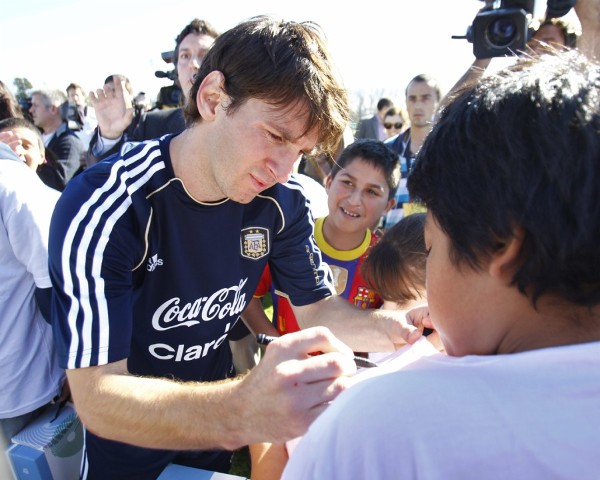 El jugador argentino Lionel Messi firma la camiseta de un niño.