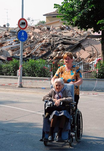 Una mujer pasea a una anciana en silla de ruedas delante de la montaña de escombros en la que quedó reducida una vivienda tras los fuertes terremotos registrados ayer.