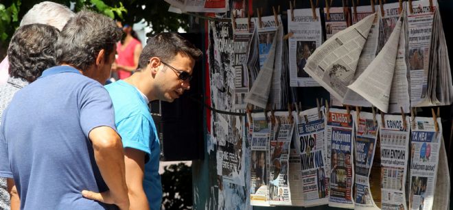 Un grupo de personas repasan los titulares de distintos periódicos en Atenas.
