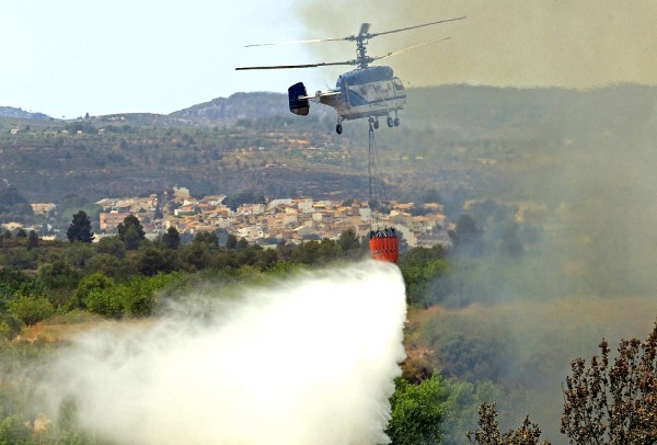 Un helicóptero realiza una descarga de agua sobre una zona de campos de cultivo cercanos a la localidad de Turis.