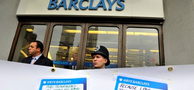 Un policía británico y un guardia de seguridad vigilan tras una pancarta donde los manifestantes pegan mensajes frente a una sucursal de Barclays.