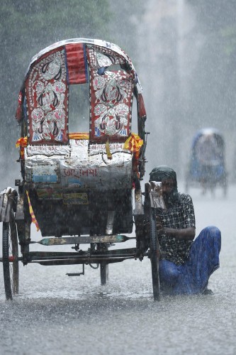Un conductor de rickshaw limpia su coche bajo la lluvia.