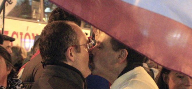 Dos hombres se besan bajo una bandera arcoiris.