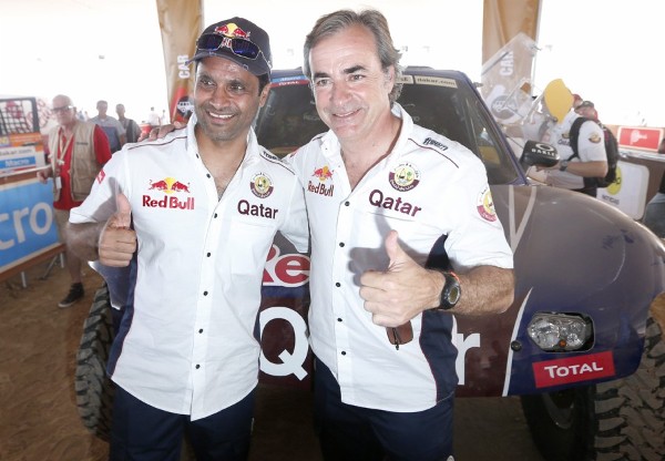 2013. El piloto español Carlos Sainz (d) y el catarí Nasser Al Attiyah Prohens posan durante las verificaciones técnicas de sus coches en el campamento del rally Dakar.