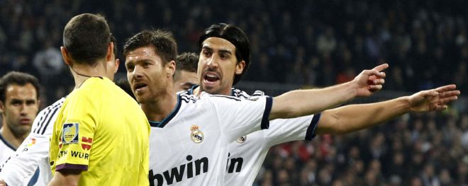Los jugadores del Real Madrid Xabi Alonso y Shami Khedira,detrás, pretestan una jugada al colegiado Carlos Clos Gómez.