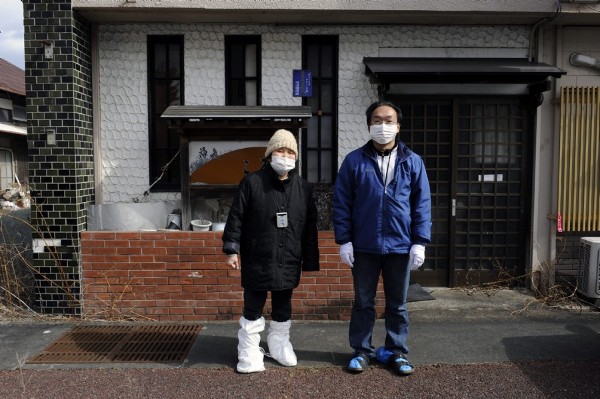 Vestidos con trajes y máscaras protectoras, Takamasa Watanabe (dcha) de 53 años y su madre, Kazuko de 79, posan para el fotógrafo frente a las puertas de su casa en una calle desierta de la abandonada localidad de Namie, en la prefectura de Fukushima.