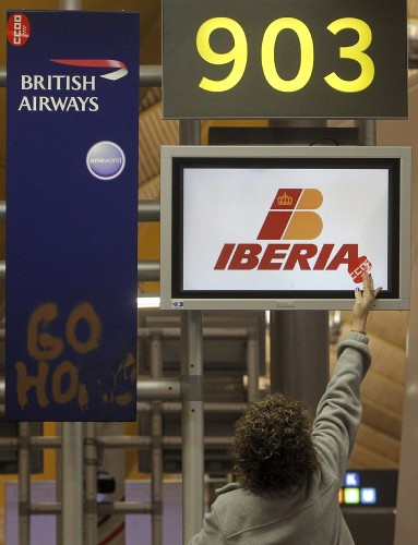 Un persona pone una pegatina de CCOO en una pantalla de Iberia junto a un cartel de British Airways, filial de la aerolínea española en el grupo IAG, con la pintada 