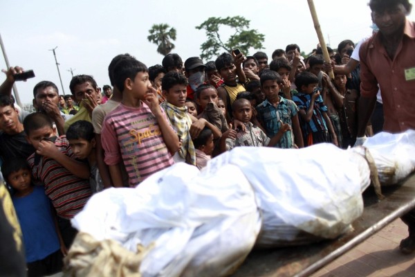 Un grupo de niños se tapa la cara mientras trabajadores cargan con un cadáver que será enterrado en una tumba de Jurain, en Daca.