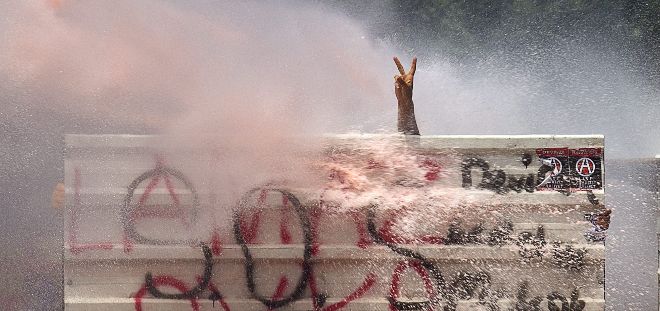 Un manifestante turco asoma la mano tras una barricada para hacer el signo de la paz mientras los antidisturbios apuntan un cañón de agua a presión hacia él.