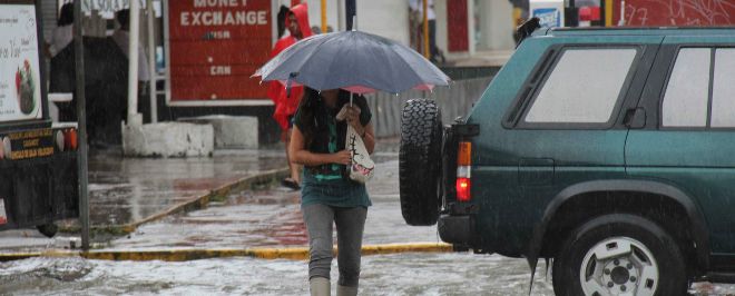 Una mujer atraviesa un calle con un paraguas en Acapulco.