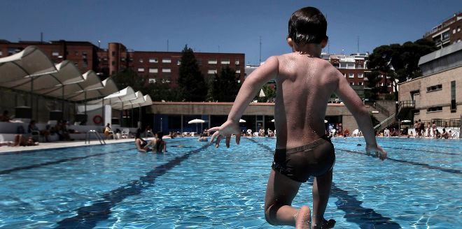 Un niño salta al agua en la piscina municipal al aire libre.