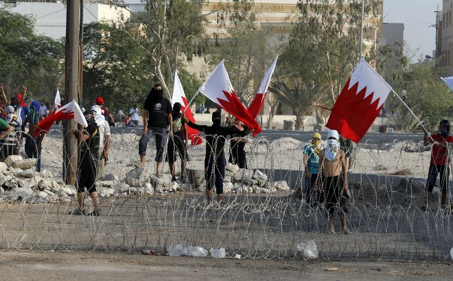 Un grupo de manifestantes sujetan la bandera bareiní tras un alambre de púas durante las protestas contra el gobierno el 14 de agosto de 2013, en Manama, Bahrein. Los manifestantes opositores bareiníes, que reclaman una reforma política y más libertad para la mayoría chií, tomaron las calles del reino bajo el lema 