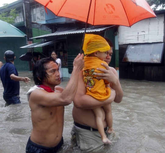 Dos hombres protegen a un bebé mientras cruzan una calle completamente inundada.
