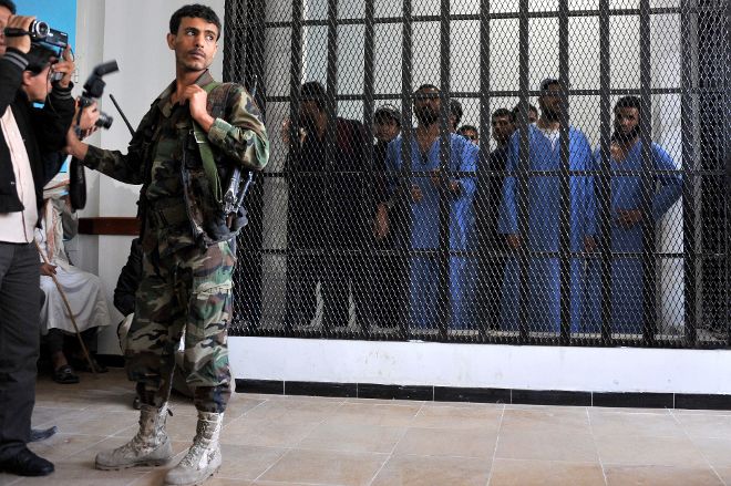A Yemeni soldier obstructs photographers as suspected al-Qaeda militants stand behind bars during their first hearing at the state security court in Sanaía, Yemen, 10 November 2013. Reports state eight alleged al-Qaeda militants were charged with the attempt to assassinate Yemeni President Abdo Rabbo Mansour Hadi.