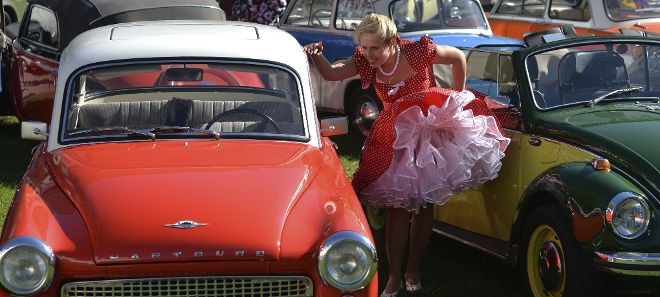 Una mujer vestida con un traje de mediados de S. XX observa un coche antiguo.