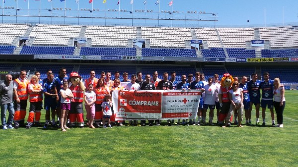 La plantilla del CD Tenerife y el voluntariado de Cruz Roja en el estadio Heliodoro Rodríguez López, junto al cartel de la campaña del Sorteo de Oro.