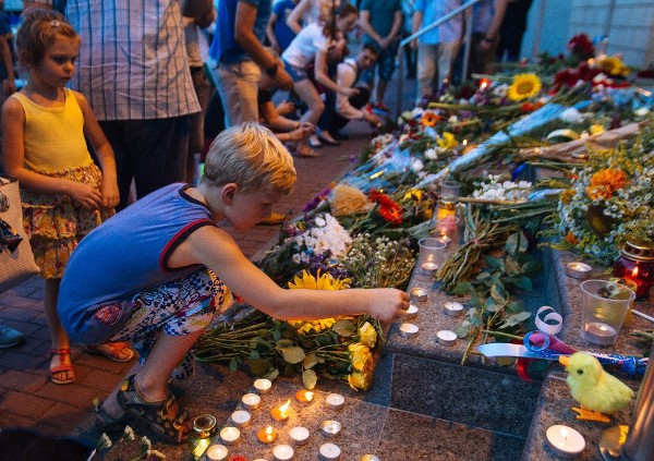 Un niño enciende una vela entre ramos de flores en conmemoración de las víctimas del avión estrellado de Malaysia Airlines al este de Ucrania.