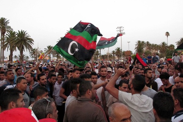 Manifestantes libios sostienen carteles y banderas nacionales mientras gritan consignas en Trípoli.