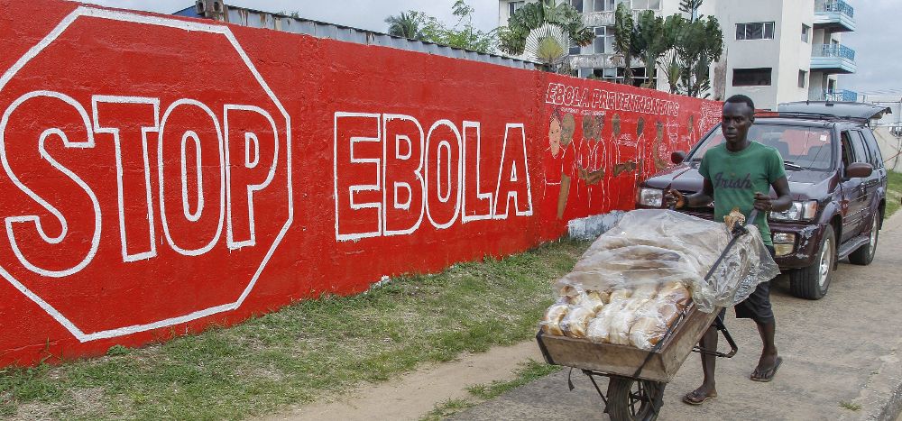 Un hombre lleva pan junto a un muro en con un anuncio de la campaña crada para combatir el brote de ébola en África Occidental, en Monrovia, Liberia.