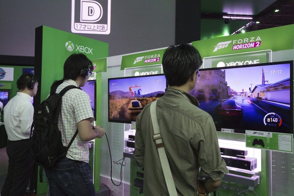 Algunos visitantes juegan a un videojuego de carreras de coche en consolas Xbox One durante la Feria de Videojuegos de Tokio 2014.