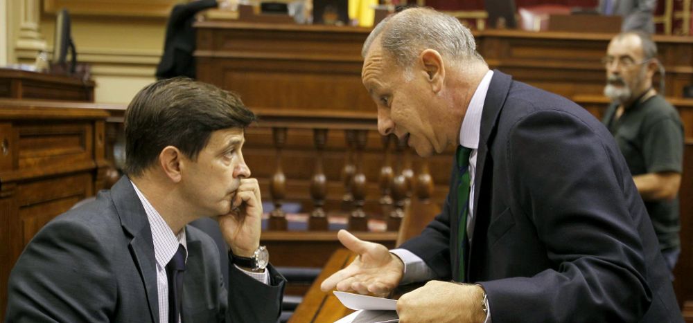 El consejero de Economía y Hacienda del Gobierno de Canarias, Javier González Ortiz (i), conversa con el diputado del PP Jorge Rodríguez, al inico del pleno del Parlamento regional.