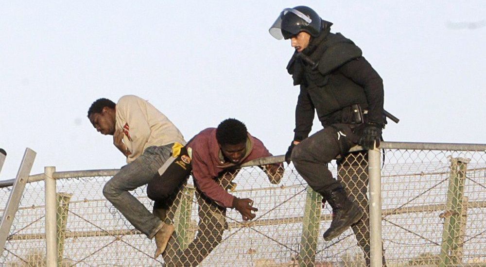 Un agente de Policía junto a dos de los ochenta inmigrantes que están encaramados desde primera hora a la valla de Melilla.