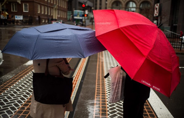 Dos mujeres caminan con paraguas bajo una leve lluvia.