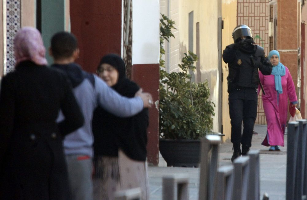 Un policía pasa junto a varios vecinos de la barriada de El Príncipe, donde la Policía española ha detenido esta madrugada a cuatro presuntos yihadistas.